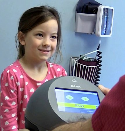 Young girl smiles as round black device with screen shows result to unseen clinician.