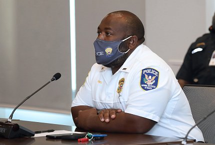 Black male in uniform and facemask, seated at conference table