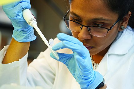 Female scientist of color wearing gloves and using pipette