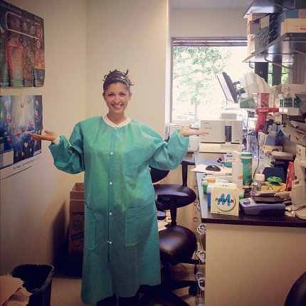 Taaffe in green protective lab smock smiles in science labroom.