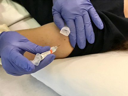 Gloved hands hold a syringe to a patient's forearm.
