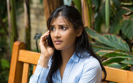 Woman with a worried expression sits on a bench and holds a phone to her ear