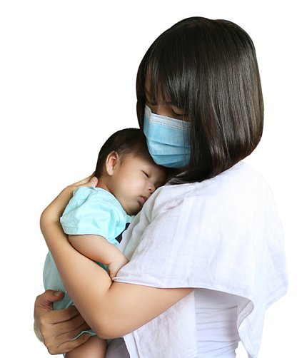 An Asian woman in a mask holds her baby, who is sleeping on her shoulder.