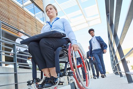 A woman travels down a city block in a wheelchair.