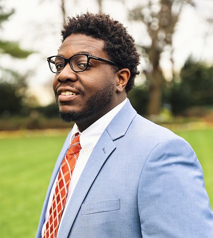 A headshot of Gilliiam, in blue suit, standing on a lawn