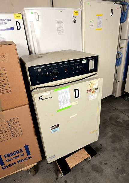 Several freezers and an incubator sit next to large packing boxes in a storage room.