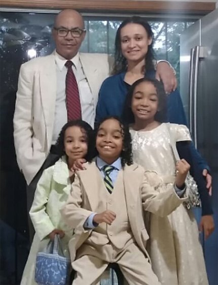 The Sant family in their kitchen, all smiles, wearing their Sunday best