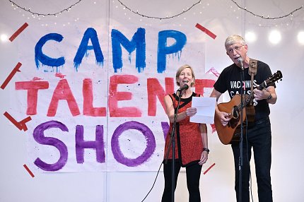 With Camp Talent Show banner in background, Baker and Collins sing at mics.