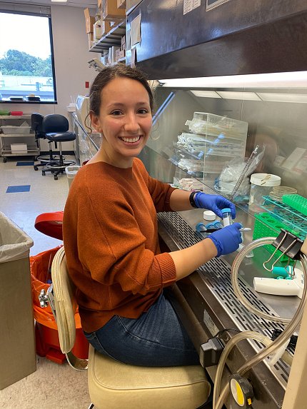 Majocha, wearing lab gloves, smiles as she's shown conducting lab work with test tubes and other equipment spread out before her.