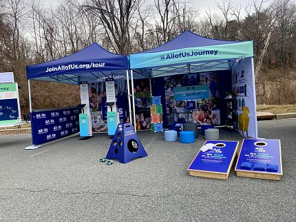 Two display tents on parking surface with All of Us banners