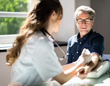An older man wearing glasses holds out his arm; nurse holds syringe to his arm.