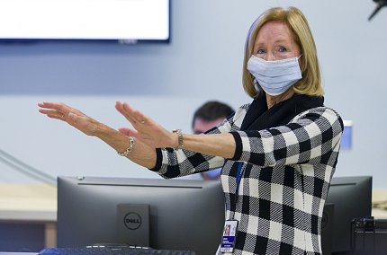 Damiano in checkered dress extends her arms straight in front of her.