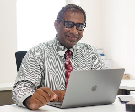 Dr. John Mathew sits with his laptop