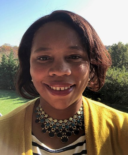 A smiling Dr. Courtney Aklin, with trees and grass behind her