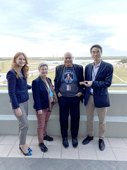 Four people smile with large green space behind them