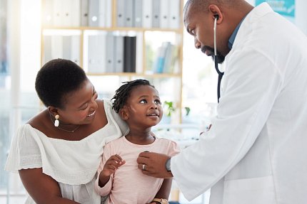 Stock image of Black mom with young daughter being examined by Black male doctor using stethoscope