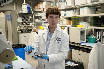 King holds a well plate and speaks to someone out of the frame