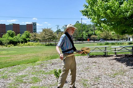 Man wearing sun hat holds shovel, with lawn and trees at his back