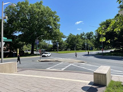 A wide intersection. One pedestrian is using the crosswalk and another is not. 