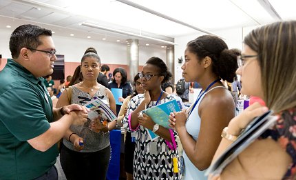 Five individuals huddled in a group, chatting and holding pamphlets