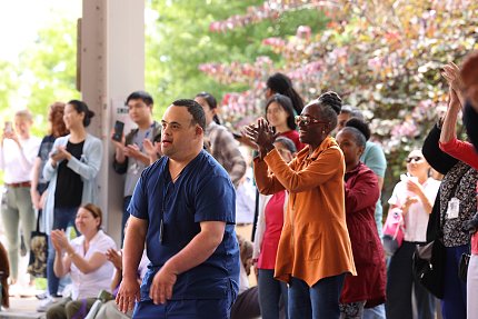 People dancing underneath a covered area with flowering trees in the background.