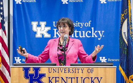 Woman speaking at podium with UK logo and backdrop