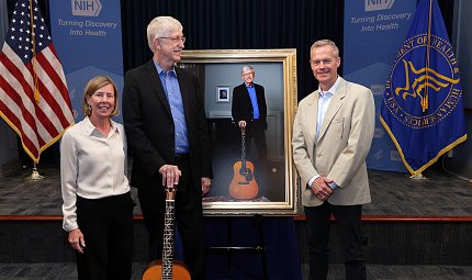 Hatfield stands next to framed photo as Collins, standing with Baker, looks at him.