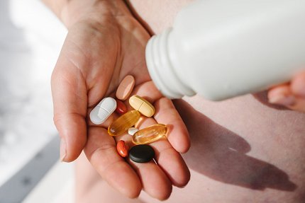 A person has shaken vitamin pills of various shapes and sizes out of a white bottle and onto their open hand.