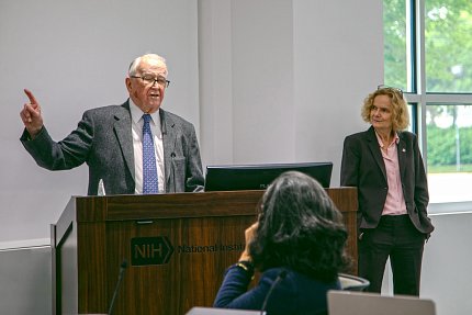Dewey gestures as he speaks at a lectern.