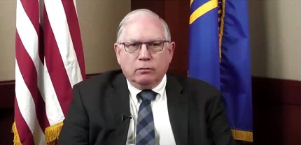 Tabak addresses viewers virtually, framed by the American and HHS flags.