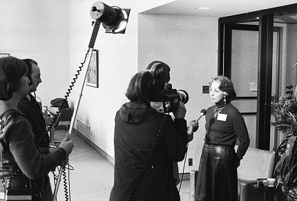 Black-and-white photo of Singer speaking to a television crew.