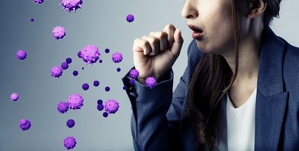 woman coughs into hand as purple bubbles representing virus particles float in front.