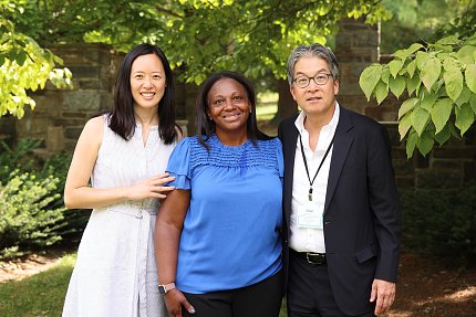Hsieh, Thomas, and Ko pose together under a tree with brick columns in the background.