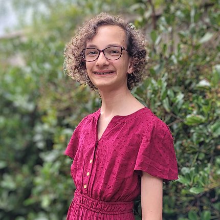 Thalia stands against a green leafy bush.