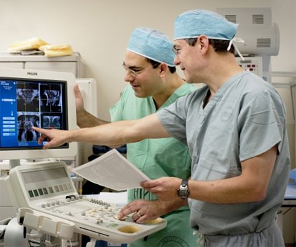 Two doctors in scrubs, one pointing to patient scans on a computer screen