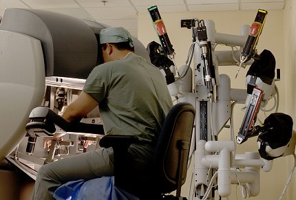 Pinto sitting, looking into large console and moving levers of surgical robot