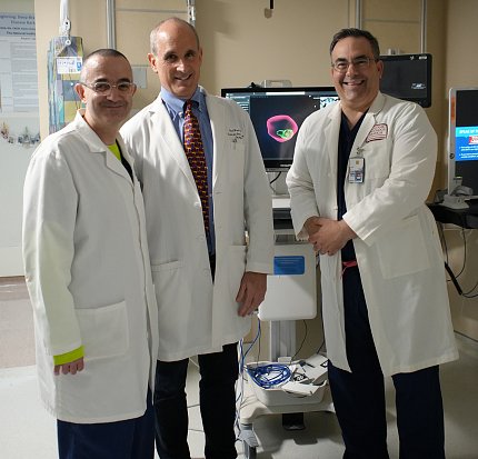 Doctors Turkbey, Wood and Pinto stand in white lab coats next to portable scanner