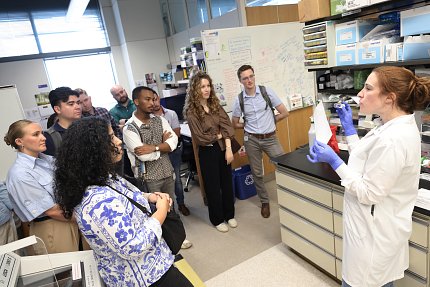 A person is showing a small vial and diagram to a group of people in a lab. 