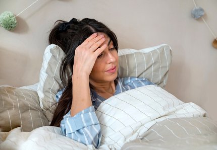Woman in striped pajamas rubs her forehead while laying in bed