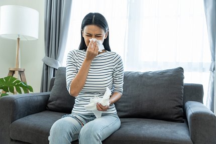 Woman seated on a couch blows her nose with a tissue