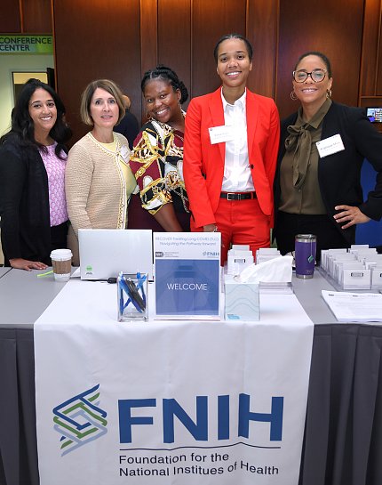 Five FNIH pose for a photo op at a table draped with an FNIH banner