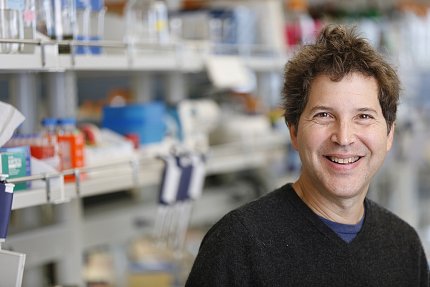 A smiling Baker stands next to shelves of lab equipment.
