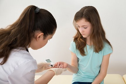 A doctor tests a child’s blood sugar with a glucometer.