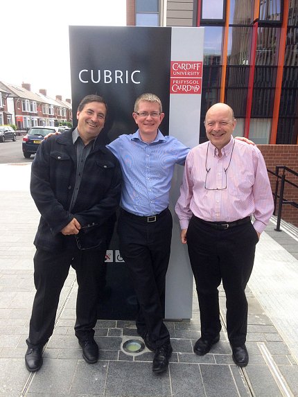 Basser and two friends pose for a photo in front of a black sign. "CUBRIC" is spelled out in white letters on the sign.