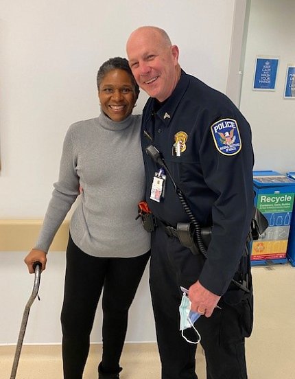 A smiling Williams standing with a cane hugs Officer Sugrue.