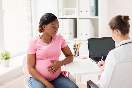 A pregnant mother in a pink top speaks with a doctor.