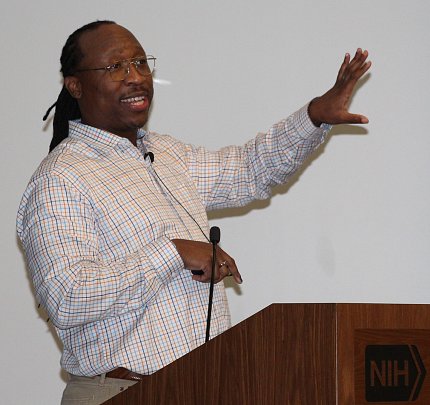 Platt stands at podium with hand extended to screen behind him.