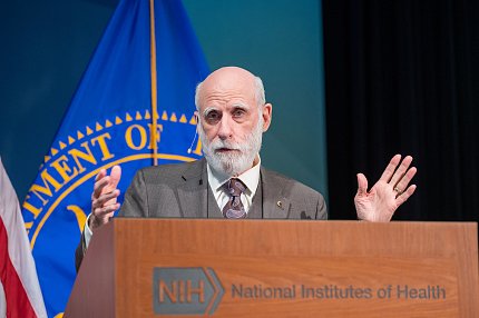 Cerf gestures at the podium, with Public Health Service flag behind him.