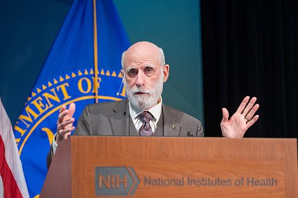 Cerf gestures at the podium, with Public Health Service flag behind him.