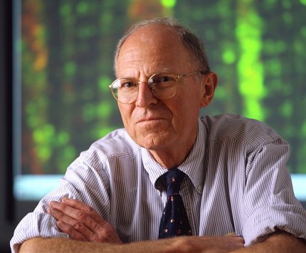 Plotz sits with his arms folded atop a surface that is out of the frame. He wears glasses and the sleeves of his shirt are rolled up past his elbows.